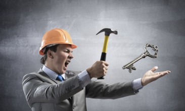 Furious businessman going to crash with hammer steel key. Young handsome contractor in business