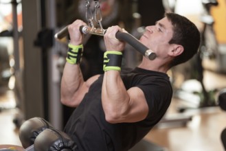 Cheerful guy training dorsal muscles by taking handles and bringing them down. Strength exercising