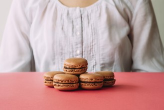Macaroons on heap on pink table against woman. Selective focus