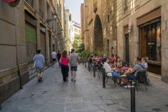 08-28-2022 Barcelona, SP People walking and sitting in cafe of Barcelona at narrow street in shadow
