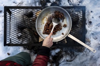 Preparing food in a pan over an open fire in the snow, Yukon, Canada, North America
