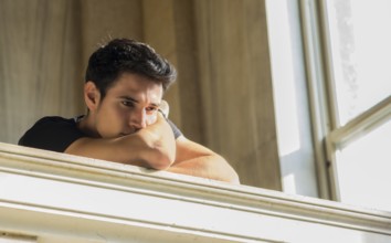Portrait of Shy Attractive Young Man Leaning on Folded Arms Against Polished Marble Staircase