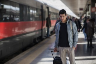 Handsome young male traveler in train station with trolley suitcase, looking down