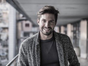 One handsome young man in urban setting in European city, standing and smiling to camera happy