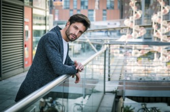 One attractive man in urban environment in city, leaning on handrail, wearing cardigan