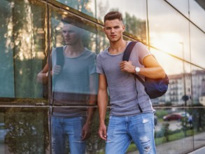 Handsome young man walking in city with backpack on shoulders, wearing t-shirt