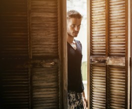 Portrait of handsome young man with beard entering the room with wooden doors