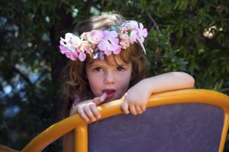 Happy childhood concept. Charming curly little girl in a wreath of flowers resting in a chair in