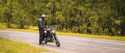 Motorcyclist checking their phone on a roadside near a forest