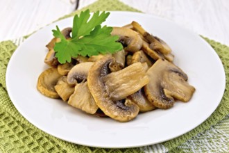 Champignons fried in a plate with a leaf of parsley on a napkin on the background light wooden