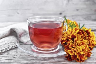 Marigold herbal tea in a glass cup and saucer, fresh flowers, burlap on wooden board background
