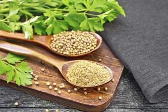 Coriander seeds and ground in two spoons, green fresh cilantro and a napkin on wooden board