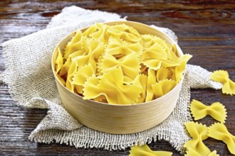 Farfalle pasta in a bark box on sackcloth on a wooden board background