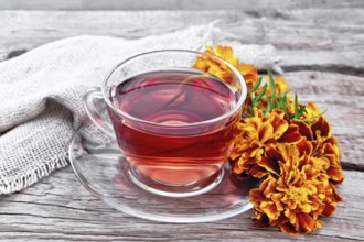 Marigold herbal tea in a glass cup and saucer, fresh flowers, sackcloth napkin on wooden board