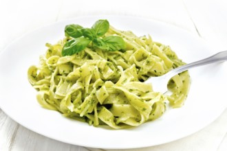 Tagliatelle pasta with pesto, basil and fork in a plate on a napkin against the background of light