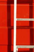 Close-up of the body of a fire engine in the sunshine with a ladder casting a shadow