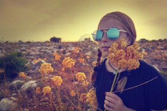 Blond country girl with sunglasses and flowers at sunset outdoor mountain