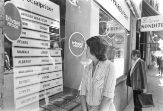 In the shop window of a travel agency. A woman is seen looking at the sign and information of the