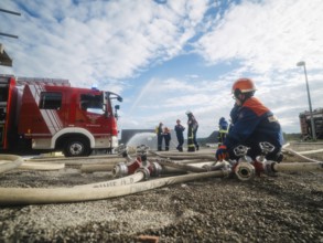 Fire engine and firefighters training, surrounded by hoses under a blue sky