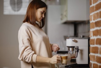Woman adding milk to coffee using an espresso machine in the kitchen