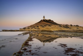 A view of the Cabo de la Huerta lighthouse at sunrise with reflections in tidal pools in the