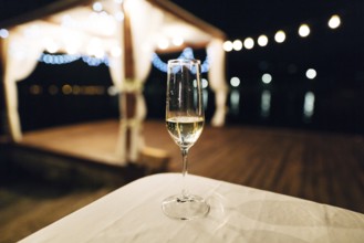 A glass of champagne stands on the table against the backdrop of a party on the beach. Beach talk