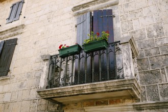 Stone balcony with a wrought iron lattice with flowerpots on the stone facade of the house.