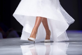 Female model walks the runway in white dress during a Fashion Show. Legs and shoes only. Fashion