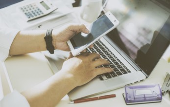 Businessman hand using smart phone and keying the data to laptop, mobile payments online shopping