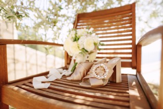 Close-up of a wooden chair with a round buckle clog and a bouquet of flowers under an olive tree.