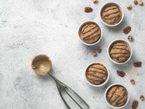 Safe-to-eat raw monster cookie dough in small portion bowl, ice cream scoop and nuts on gray cement