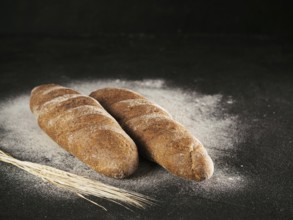 Two whole homemade rye loaf bread with buckwheat flour on black textured background. Copy space.