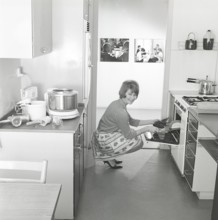 In the kitchen in the 1960s. A young woman in the kitchen taking out the ready baked breads from