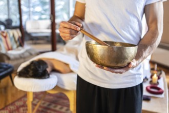 Massage therapist standing with a singing bowl in hands and giving a sound massage, to his client