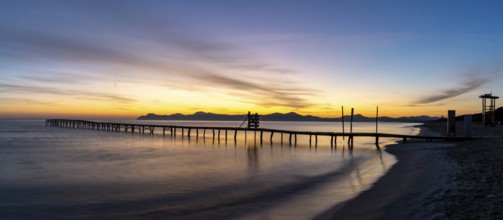 Peaceful sunrise seascape with an old wooden dock leading out into the calm ocean waters of Alcudia