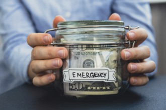 Female hands Saving Money In Glass Jar filled with Dollars banknotes. EMERGENCY transcription in
