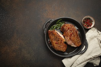 Two roasted duck breast fillets with crispy skin, with pepper and rosemary, top view in black cast
