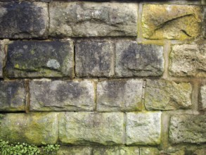 An old grey damp stone wall made of large regular blocks covered in patches of moss