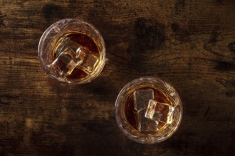 Whiskey in glasses with ice. Bourbon whisky on rocks on a dark rustic wooden background, overhead