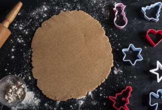 Black wooden table above view with multicolored cookie cutters and gingerbread batter
