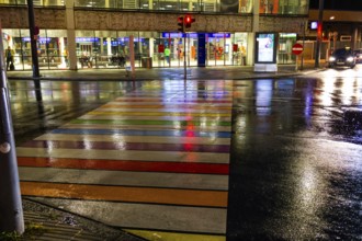 Rainy asphalt, zebra crossing in rainbow colours leads to the station, night shotLeoben, Styria,