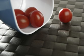 Group of cherry tomatoes falling from blue bowl over brown tablacloth