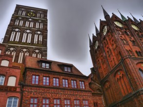High gothic church towers and brick clock tower, surrounded by historic buildings under a gloomy