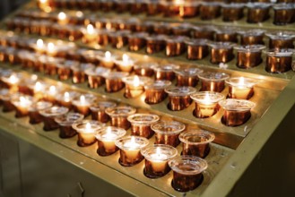 Votive candles burn in rows on a stand in the temple. Close-up.