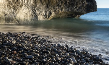 Low angle view of seascape with windy waves splashing on the rock and the sea pebbles. Rock of