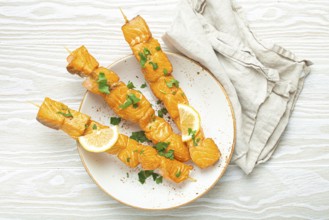 Grilled barbecue salmon skewers seasoned with green parsley and lemon on ceramic plate on white