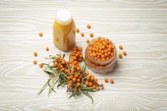 Sea buckthorn healthy drink in bottle, ripe berries in glass jar and branches with leaves top view