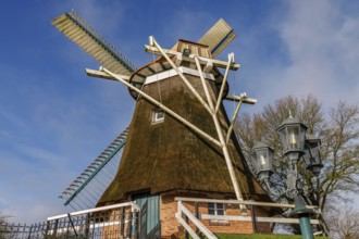 Traditional windmill next to antique looking lanterns against a blue sky, burlage, east frisia,