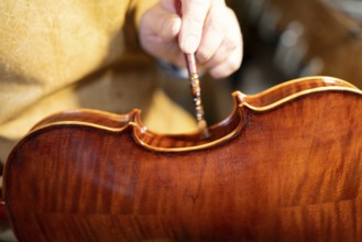 Luthier carefully varnishing a violin with a brush, showcasing the craftsmanship and meticulous