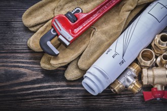 Safety gloves monkey wrench blueprints brass plumbing connectors gate valve on wooden board